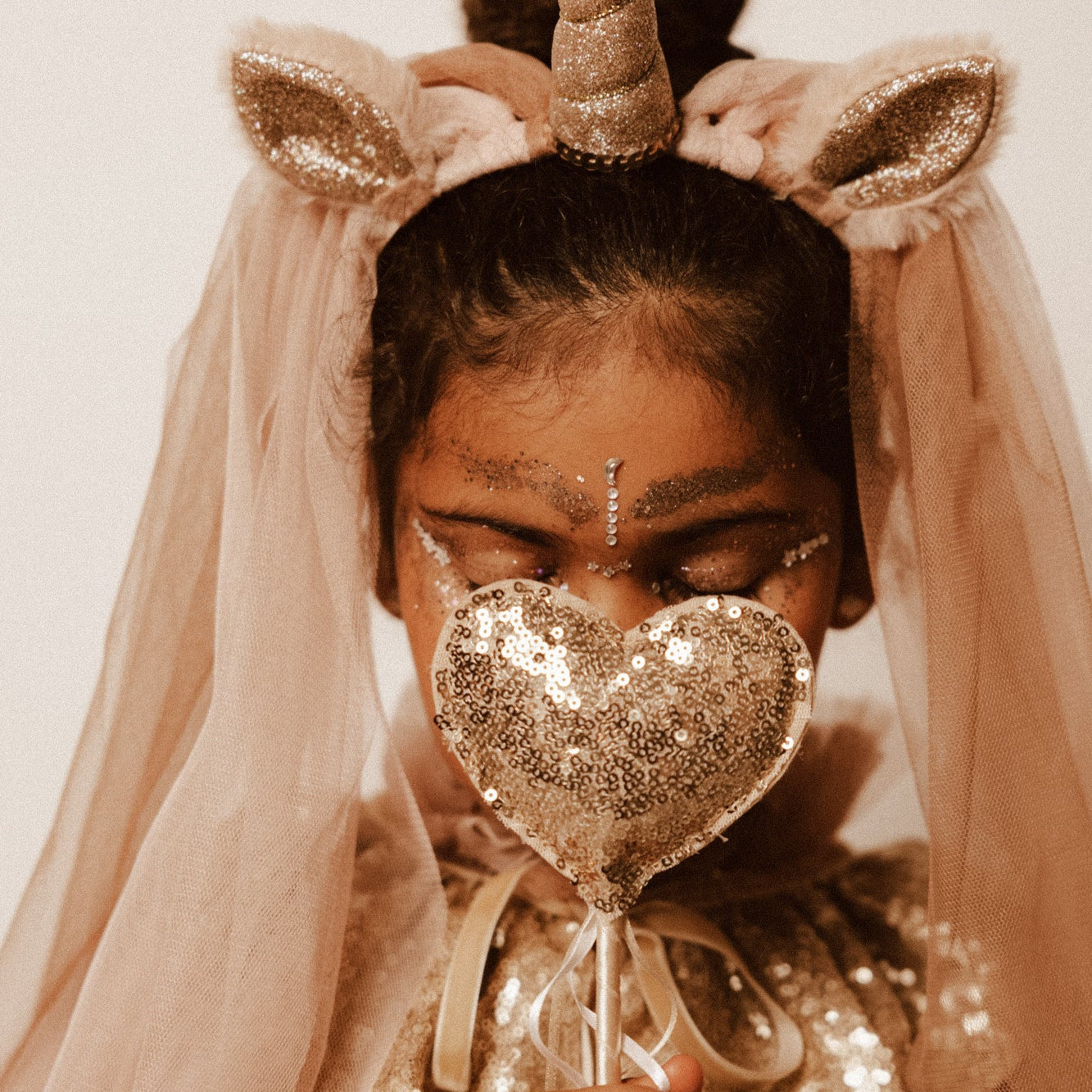 Criança de 7 anos vestida com um disfarce cor-de-rosa de unicórnio , com uma varinha mágica em forma de coração.