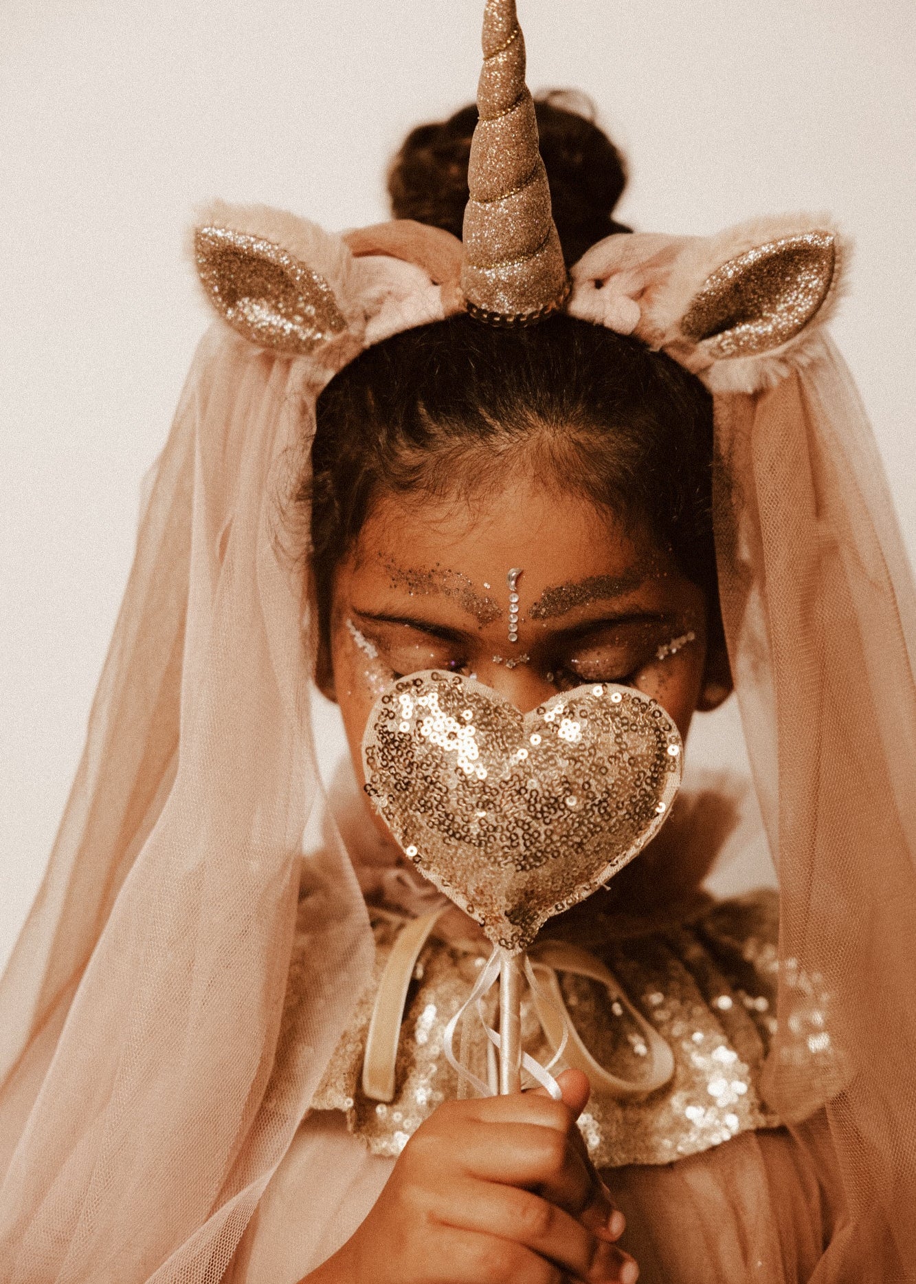 Criança de 7 anos vestida com um disfarce cor-de-rosa de unicórnio , com uma varinha mágica em forma de coração.