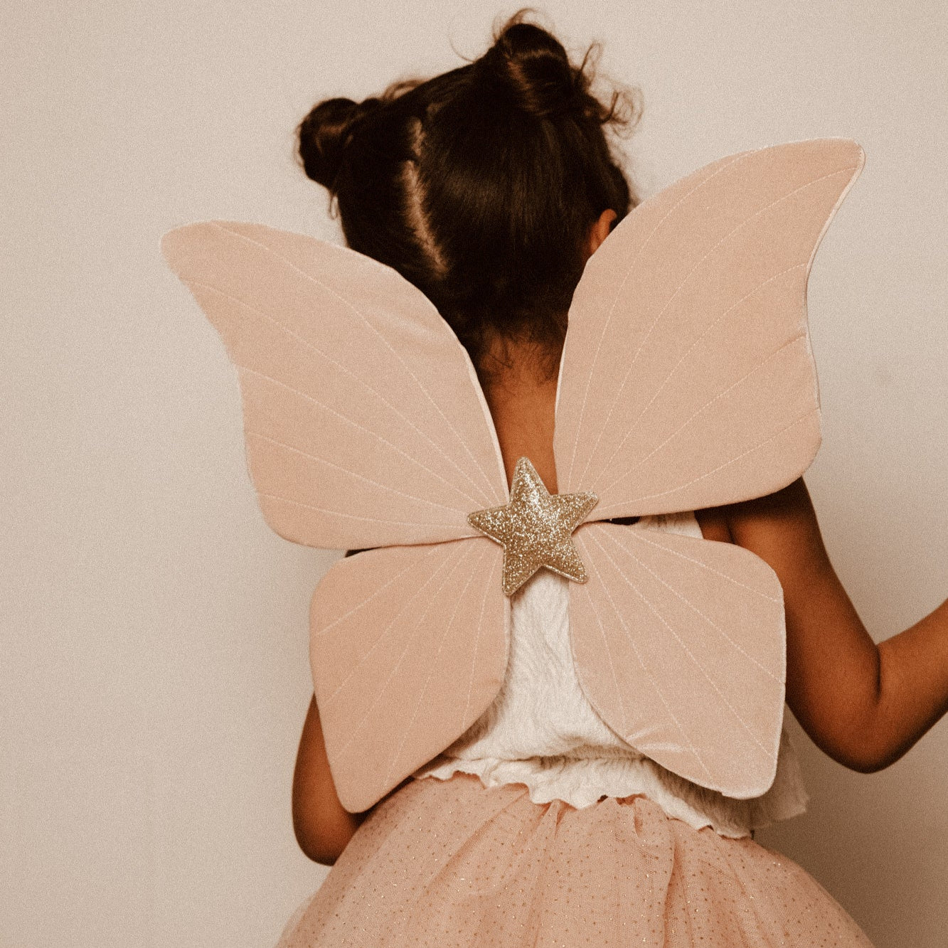 Criança de 5 anos vestida com um disfarce cor-de-rosa de borboleta, com uma varinha mágica em forma de estrela com purpurinas e glitter.