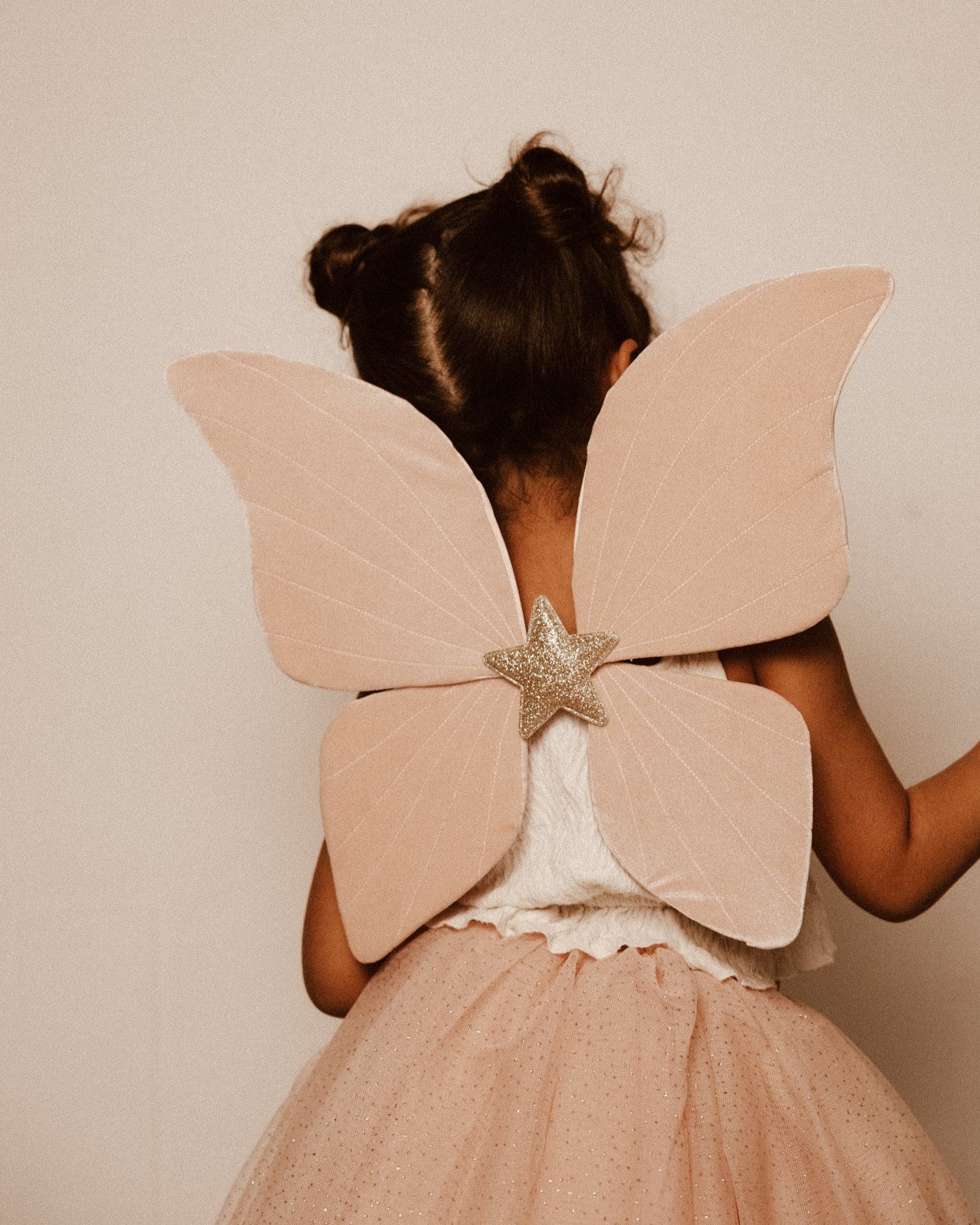 Criança de 5 anos vestida com um disfarce cor-de-rosa de borboleta, com uma varinha mágica em forma de estrela com purpurinas e glitter.